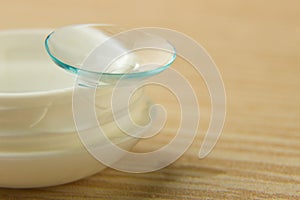 Contact lenses for the eyes and a white container with a solution on a wooden table photo