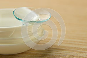 Contact lenses for the eyes and a white container with a solution on a wooden table