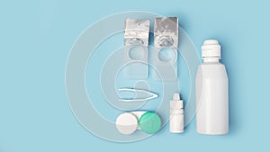 Contact lenses set with saline in bottle, tweezers, eye drops, plastic case with solution on blue