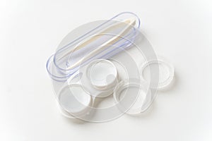Contact lenses are in a solution in a container for contact lenses and tweezers in a case against a light background. Contact