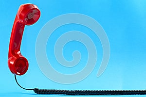Contact us concept and floating phone receiver with a vintage red telephone handset floating above the curly cable isolated on