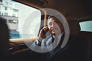 Contacting clients in commute. a mature businessman using his phone while traveling in a car.