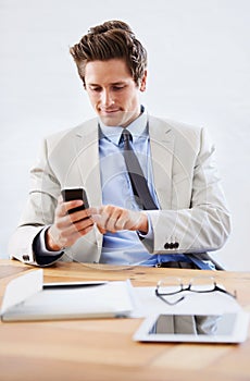 Contacting a colleague. A young businessman sending a text message from his desk.