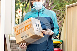 Contactless delivery during COVID-19 pandemic lockdown concept. Delivery man wearing mask and gloves holds a parcel with medical