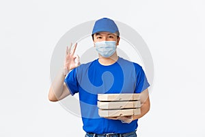 Contactless delivery, covid-19 shipping, preventing virus concept. Cheerful asian male courier in blue uniform, medical