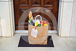 Contactless food delivery service concept. Paper bag with groceries delivered and left outside at entrance door.  Online shopping.