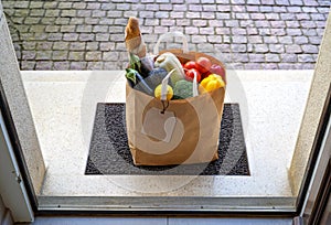 Contactless food delivery service concept. Paper bag with groceries delivered and left outside at entrance door. View from inside