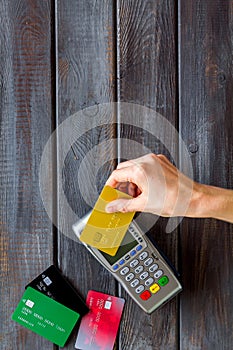 Contactless payment, paypass. Hand hold bank card near terminal on dark wooden background top-down copy space