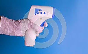 Contactless thermometer in the hand of a man in a medical glove on a light blue background. Copy space.