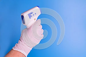Contactless thermometer in the hand of a man in a medical glove on a light blue background. Copy space.