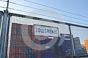 Container behind a fence with a sign saying `customs barrier` Zollgrenze in German