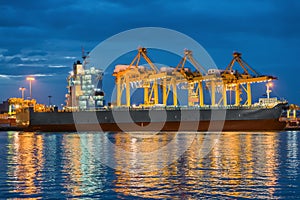 Container Cargo freight ship with working Container crane in shipyard at dusk