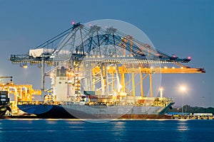 Container Cargo freight ship with working crane bridge in shipyard at dusk