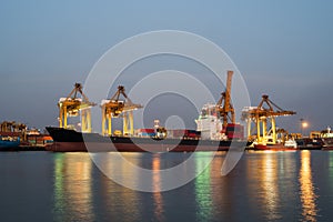 container cargo freight ship with working crane bridge in shipyard at night