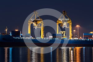 container cargo freight ship with working crane bridge in shipyard at night