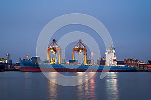 container cargo freight ship with working crane bridge in shipyard at twilight
