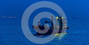 Container cargo ship with navigation lights anchored in outer anchorage of Singapore at night