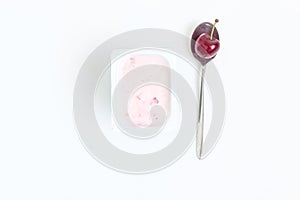 Container with cherry yogurt and spoon with one cherry berry, to