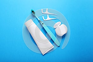 Container with dental floss, toothpaste and toothbrush on light blue background, flat lay