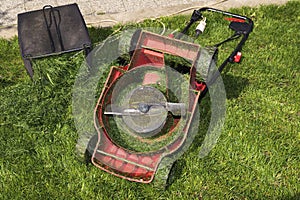 Container full of cutting grass and red mower upside down