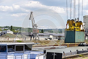 A container gantry crane on a rail loads the container into a barge standing on the banks of the river Rhine in Germany.