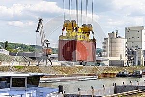 A container gantry crane on a rail loads the container into a barge standing on the banks of the river Rhine in Germany.