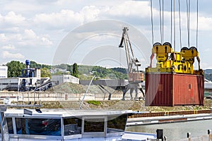 A container gantry crane on a rail loads the container into a barge standing on the banks of the river Rhine in Germany.