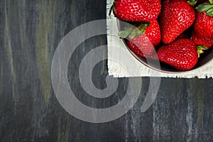 Container with healthy strawberries, grouped on the right side on a white cloth on a dark table