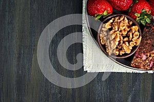Container with healthy strawberries, nuts and seed omelet, grouped on the right on a white cloth on a dark table