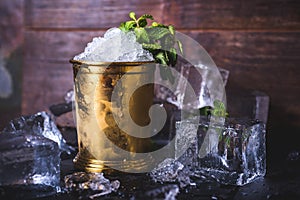 A container with ice stands among ice cubes and mint.