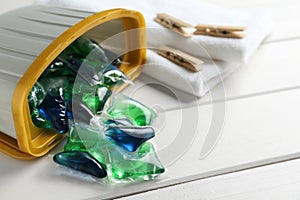 Container with laundry capsules on white wooden table