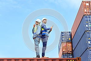 Container operator wearing white helmet and reflection shirt and holding tablet doing routine inspection while working in