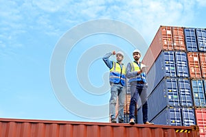 Container operator wearing white helmet and reflection shirt and holding tablet doing routine inspection while working in