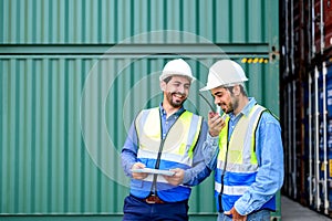 Container operator wearing white helmet and reflection shirt and holding tablet doing routine inspection while working in containe