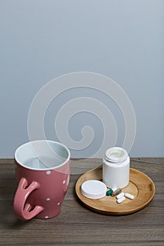 Container with pills and a mug of water. The lid of the container and several tablets are next to each other