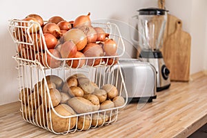Container with potatoes and onions on wooden kitchen counter. Orderly storage