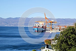 Container ship with containers to shore in port ship port on horizon / Cargo transportation by sea and goods unloading process.