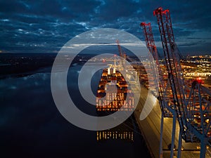 Container ship lights at dusk with crane at Southampton Docks UK aerial