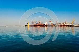 Container ship in the port on the horizon. Port crane loads a container on a ship