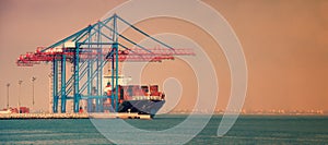 Container ship in the port on the horizon. Port crane loads a container on a ship. Cargo transportation by sea.