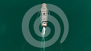 Container ship sailing full speed in green sea, aerial top view