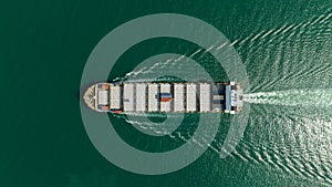 Container ship sailing full speed in green sea, aerial top view