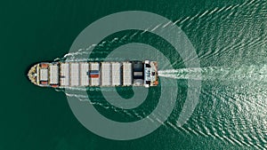 Container ship sailing full speed in green sea, aerial top view