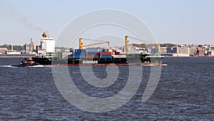 Container ship SPICA underway in New York Harbor, small tug boat katching up, Brooklyn waterfront in the background