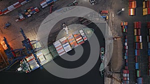 Container ship is unloading in the port in the evening aerial top down view