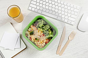 Container with tasty food, cutlery, keyboard, glass of juice and notebooks on white wooden table, flat lay. Business lunch