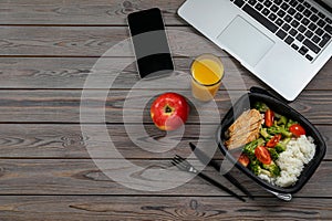 Container of tasty food, glass of juice, laptop, apple and smartphone on wooden table, flat lay with space for text. Business