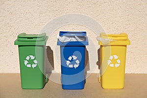 Container trash bin for recycling near grunge wall. Yellow, green, blue bins for recycle plastic, paper and glass trash