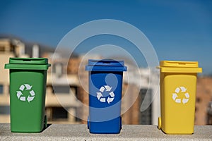 Container trash bins for recycling with city background. Yellow, green, blue bins for recycle plastic, paper and glass