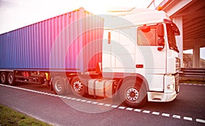 A container truck with a semi-trailer transports cargo from a port to another country along a highway in the summer